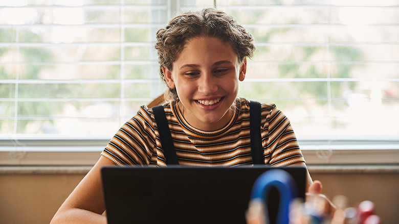 A teen girl smiles at her laptop